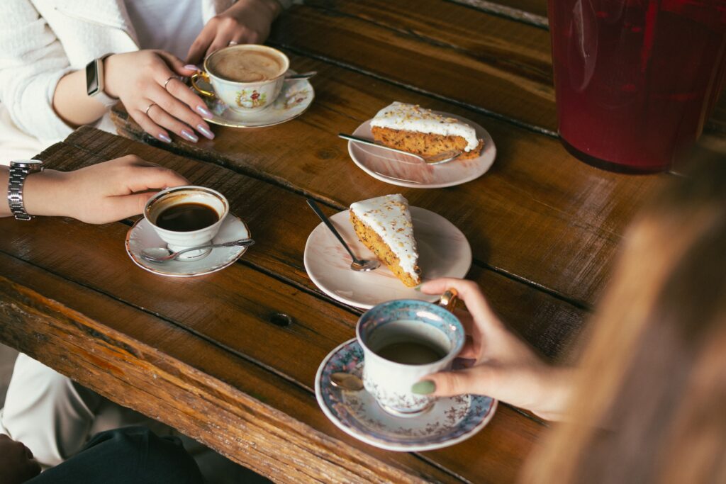 Three friends enjoying coffee and carrot cake at a rustic café setting.