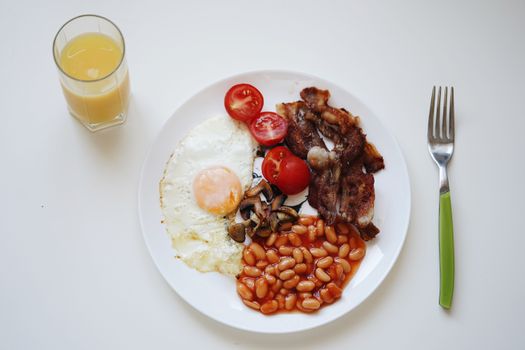 A mouth-watering breakfast featuring bacon, beans, egg, and orange juice.