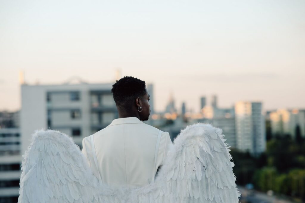 An angelic figure with white wings and suit gazes over a modern cityscape, embodying serenity.